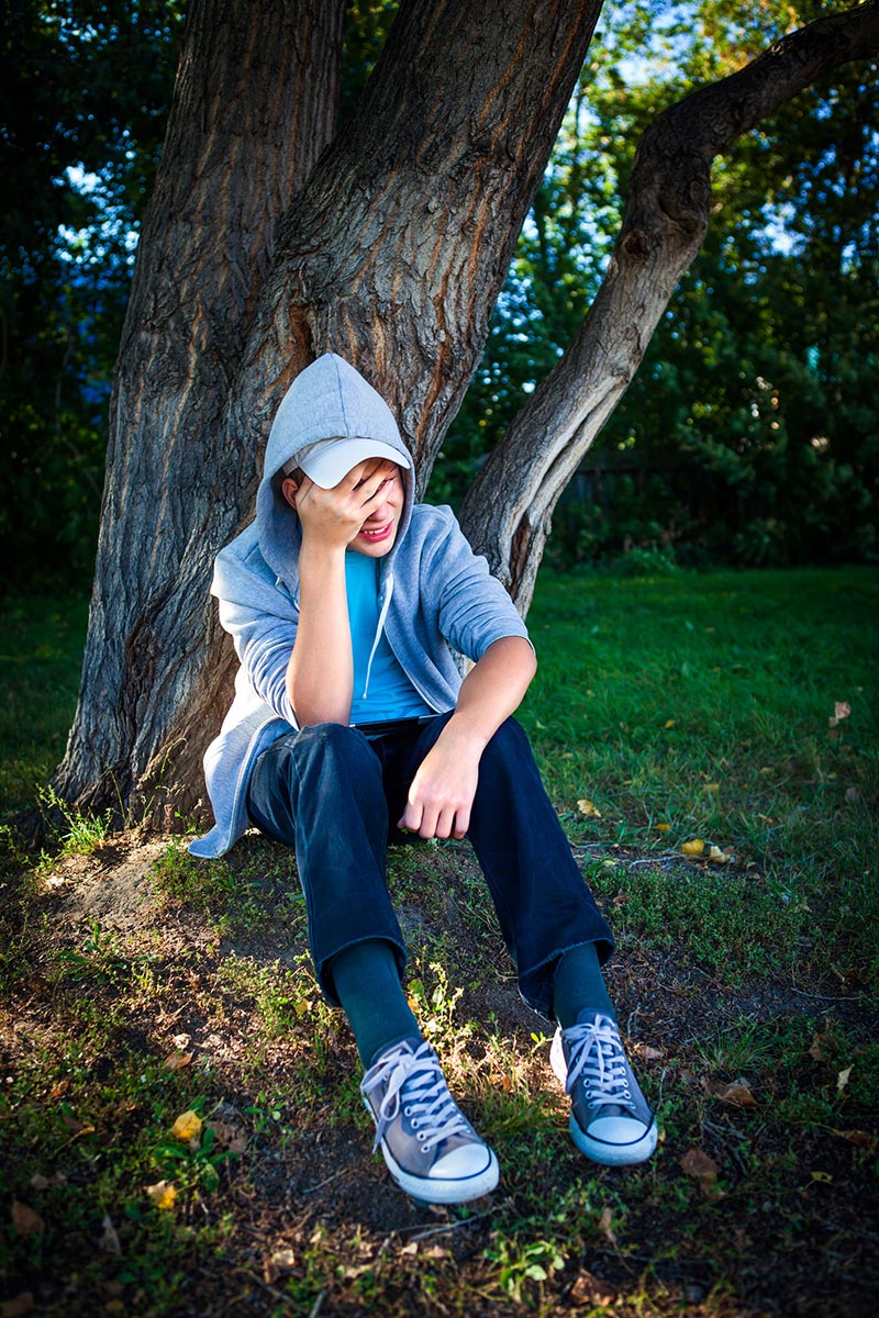 Troubled young man sitting in the shade of a tree.