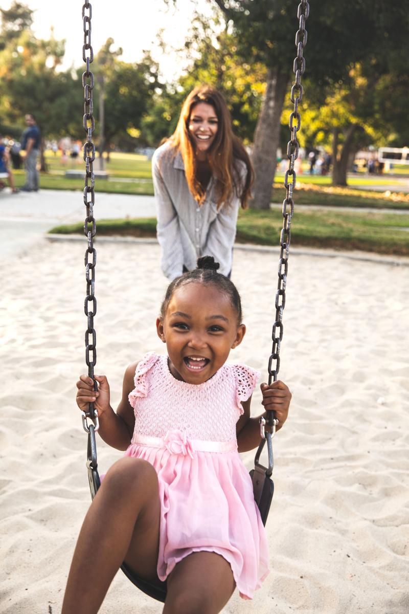 a mother smiling as she pushes her laughing child on a swing