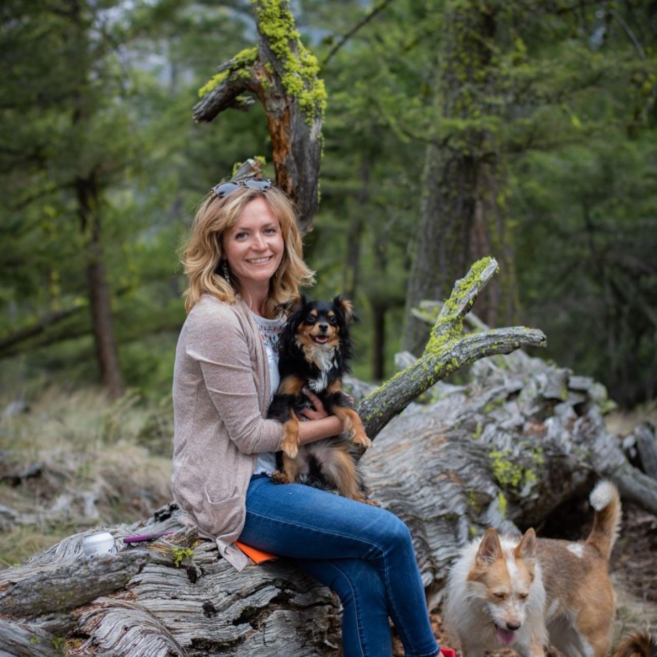 Heather Schwartz, Program Manager sitting on a log in the forest with her dogs